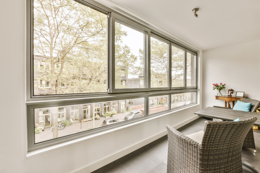 a living room with a table, chair and large window looking out onto the street in front of the house